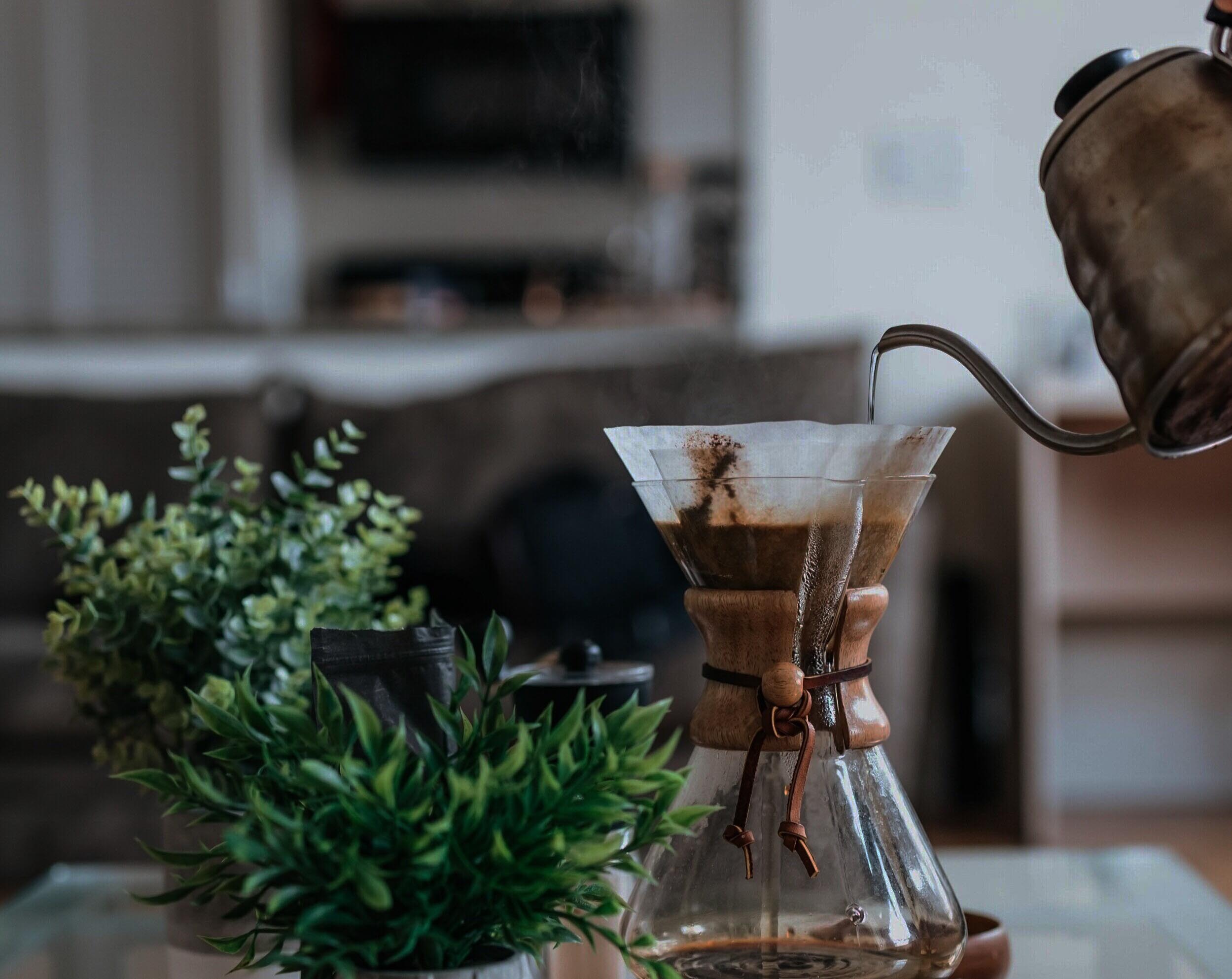 Making coffee puring ht water from a kettle into a glass coffee maker witha cone filter and grounded coffe.